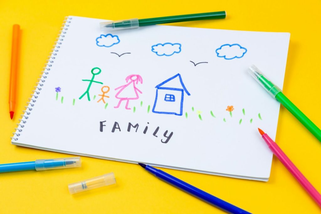ציור משפחתי של ילד על שולחן ביתי לצד כלי כתיבה